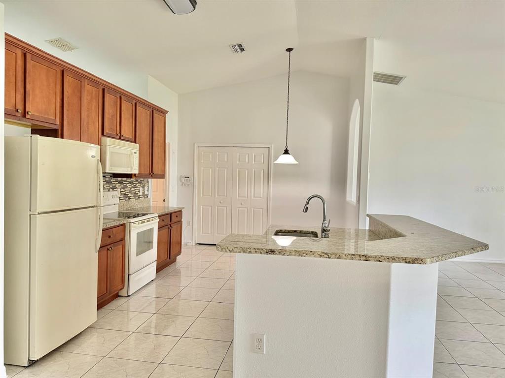 A kitchen with wood cabinets, granite countertops, white appliances, and a tiled floor — 3264 DELTONA BOULEVARD, SPRING HILL, FL