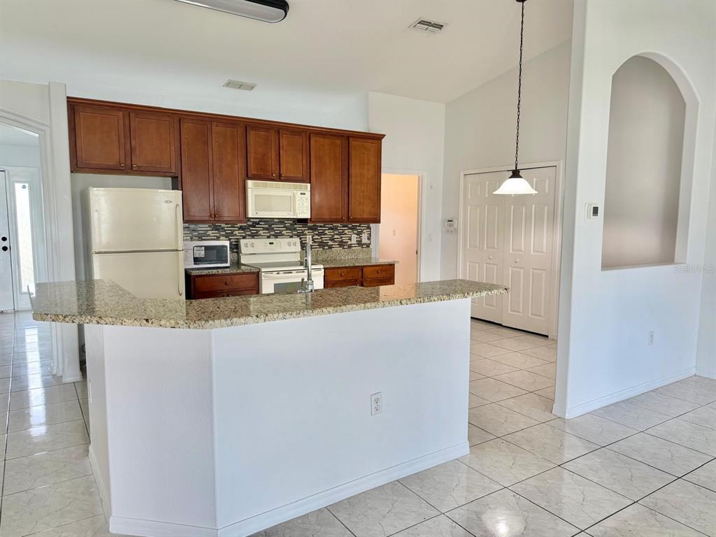 A kitchen features wood cabinets, granite countertops, white appliances, and a breakfast bar — 3264 DELTONA BOULEVARD, SPRING HILL, FL