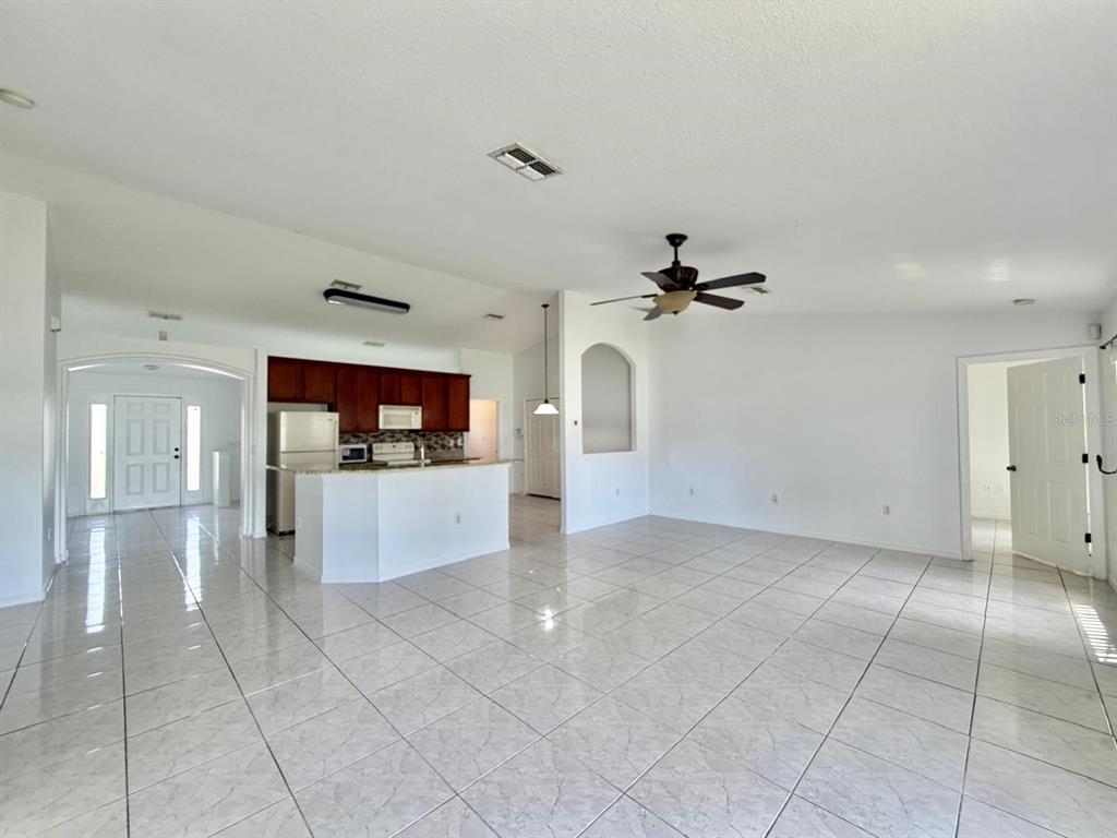 An open-concept living area features white tile flooring, a kitchen with dark cabinets, and a ceiling fan — 3264 DELTONA BOULEVARD, SPRING HILL, FL