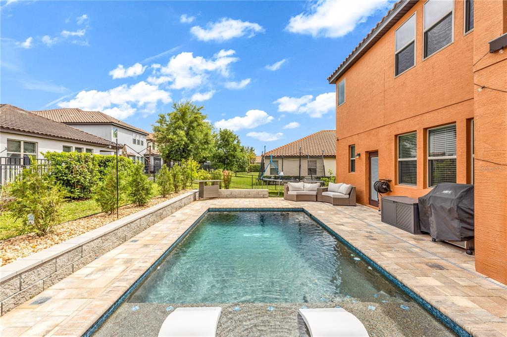 A rectangular swimming pool sits on a paved patio beside an orange two-story house — 239 LUGANO WAY, DEBARY, FL