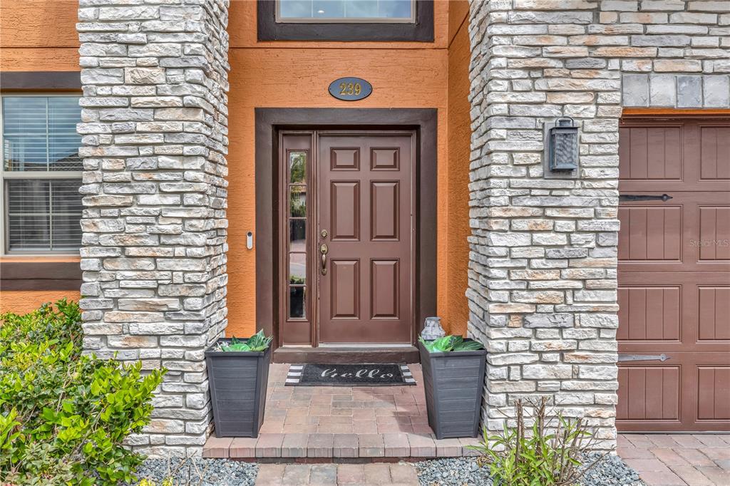 The front entrance features a brown door, stone pillars, and a welcome mat — 239 LUGANO WAY, DEBARY, FL