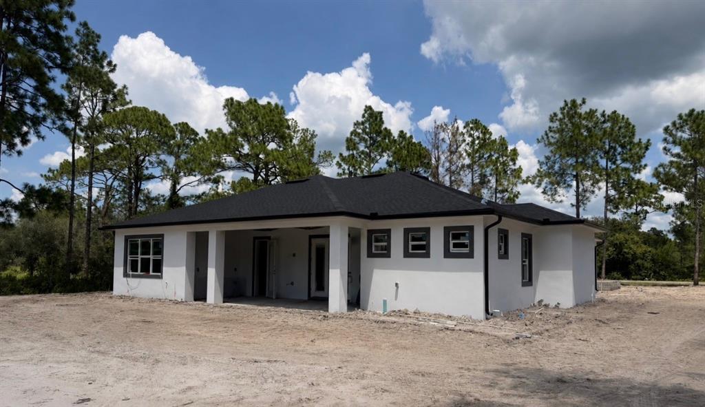 The exterior of a newly constructed white stucco house with a dark shingled roof — 40401 ROYAL TRAILS ROAD, EUSTIS, FL