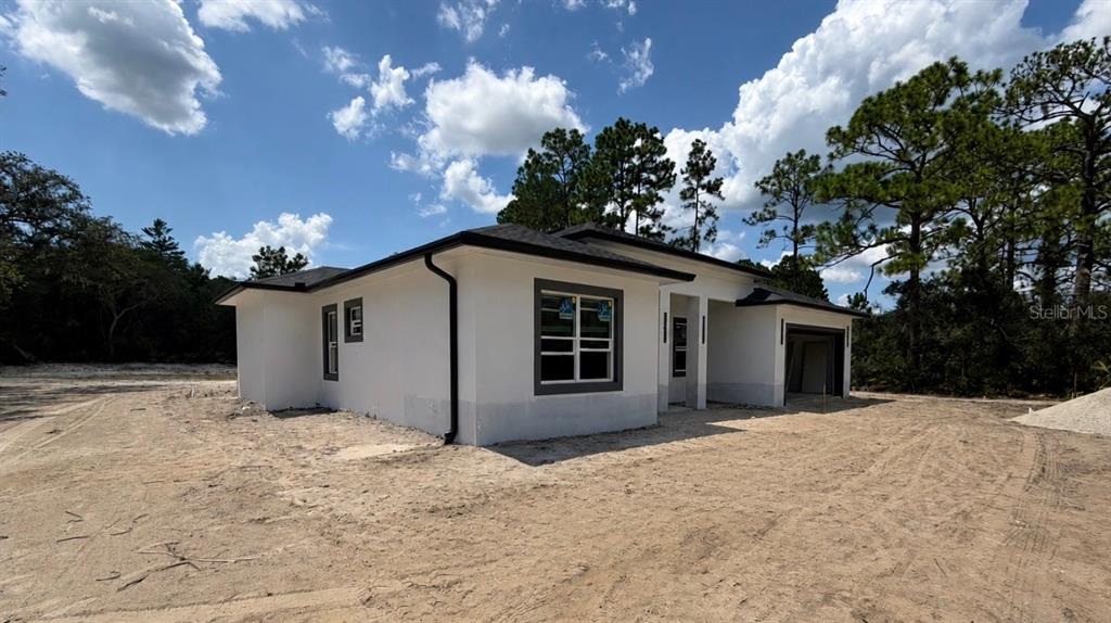 A newly constructed single-story house with white stucco walls and dark trim sits on sand — 40401 ROYAL TRAILS ROAD, EUSTIS, FL