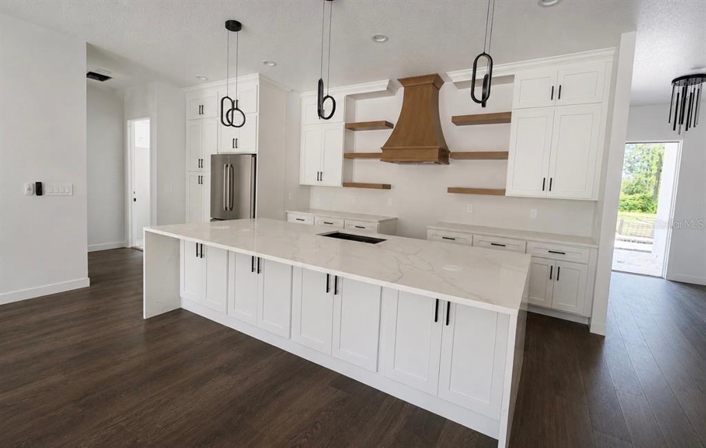A modern kitchen features white cabinetry, a large quartz island, and a wooden range hood — 40401 ROYAL TRAILS ROAD, EUSTIS, FL