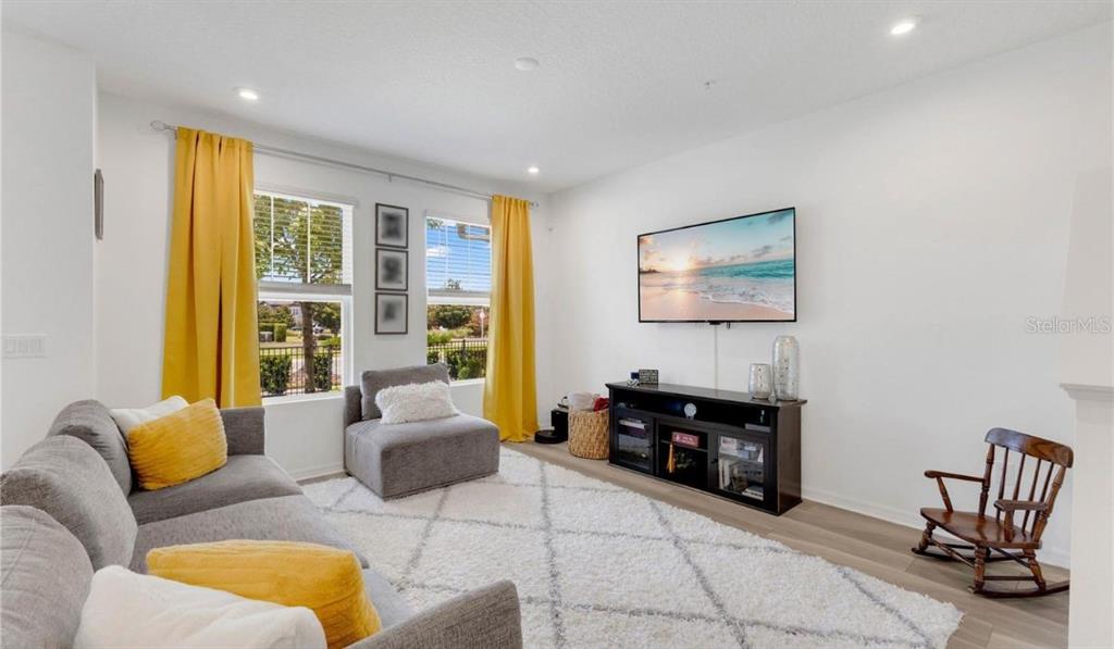 An open-concept living and dining area features light wood flooring, a gray sofa, and furniture — 9421 RANDAL PARK BOULEVARD, ORLANDO, FL