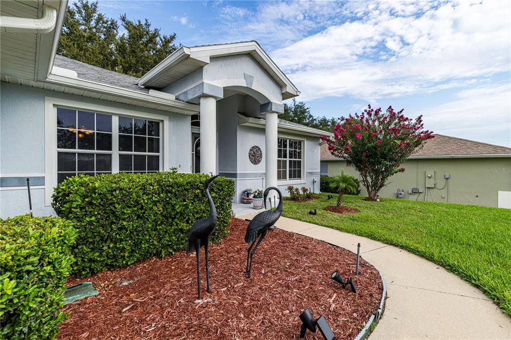 A light blue house exterior features a covered entryway with columns and two crane statues — 5154 INDIAN OCEAN LOOP, TAVARES, FL