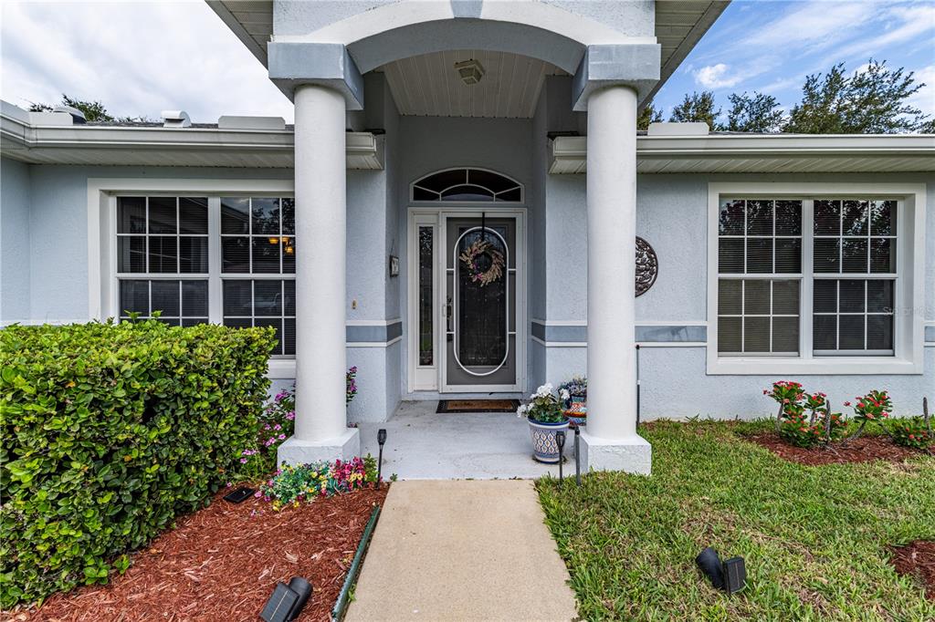 The front entrance of a light blue house features two white columns and a glass door — 5154 INDIAN OCEAN LOOP, TAVARES, FL