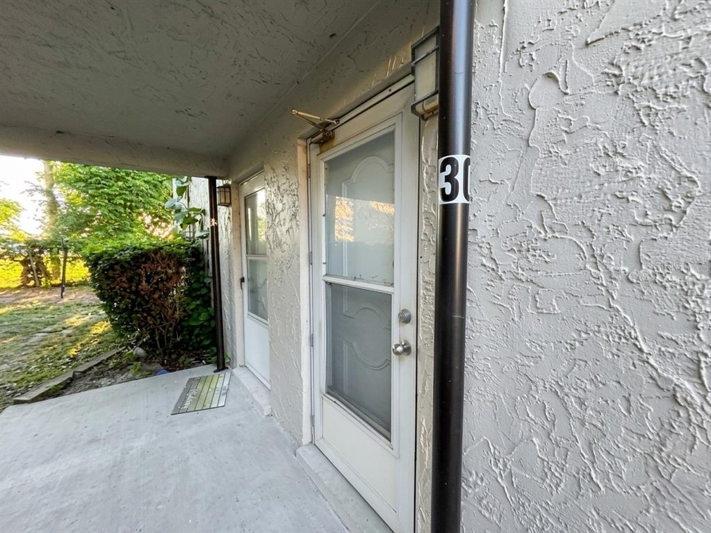 A concrete walkway leads to two white exterior doors with a black support pole nearby — 1103 CYPRESS GARDENS BOULEVARD UNIT 30, WINTER HAVEN, FL