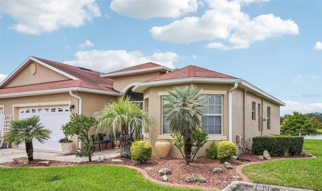 A tan single-story house with a two-car garage, red roof, and landscaped front yard — 10086 KETCH KAY LANE, OXFORD, FL