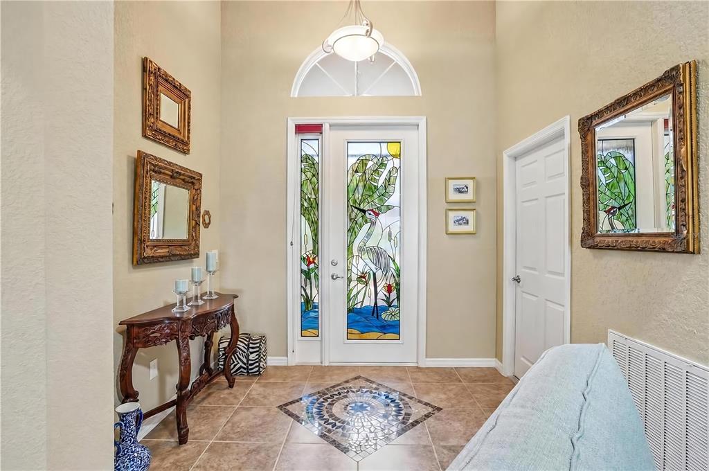 A paved walkway leads to the arched entryway of a tan stucco home with landscaping — 10086 KETCH KAY LANE, OXFORD, FL
