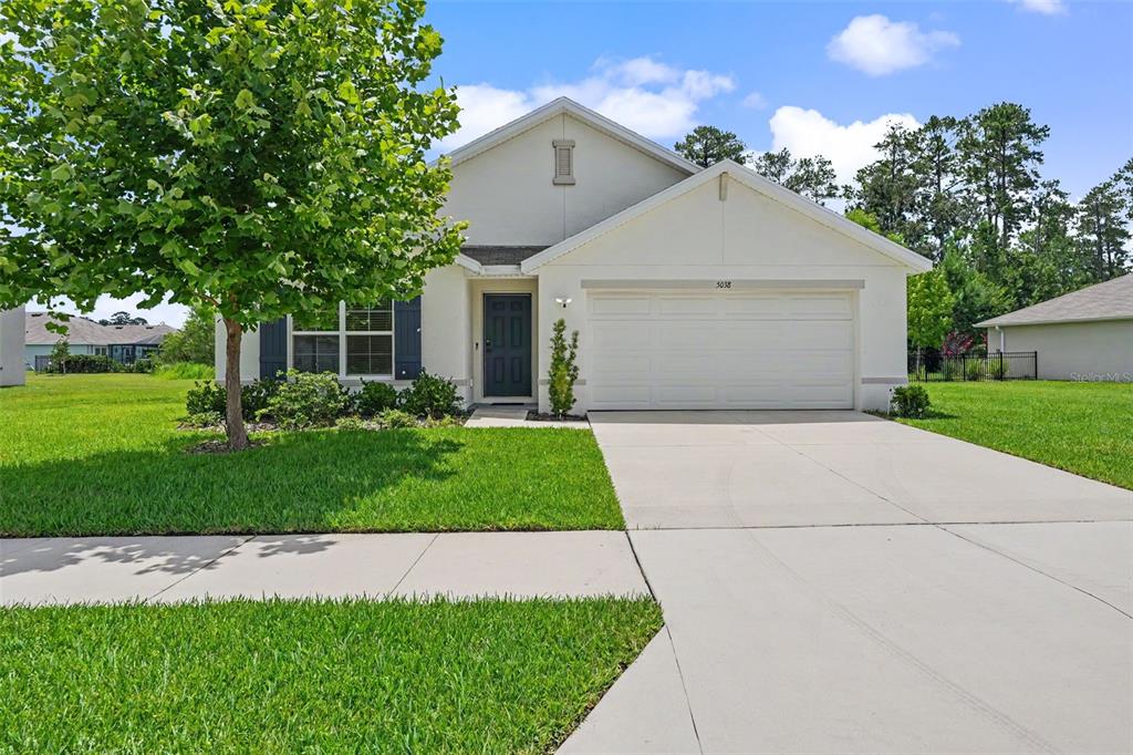 A single-story house with a white exterior, a two-car garage, and a large front tree — 5038 CADIZ COURT, BROOKSVILLE, FL