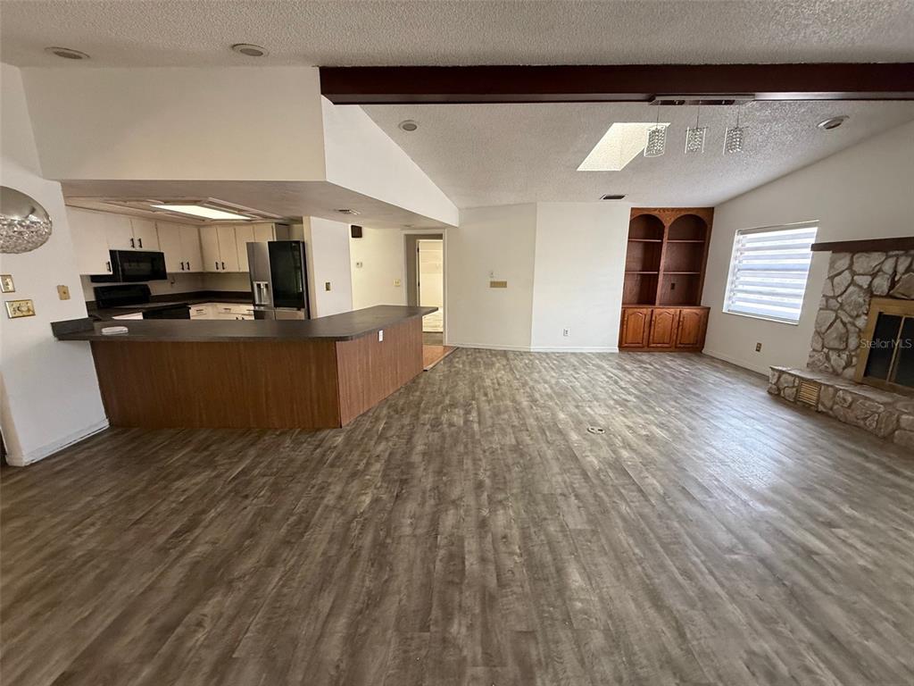 An open-concept living room features wood-look flooring, a stone fireplace, and an adjacent kitchen — 5312 SUWANNEE ROAD, WEEKI WACHEE, FL