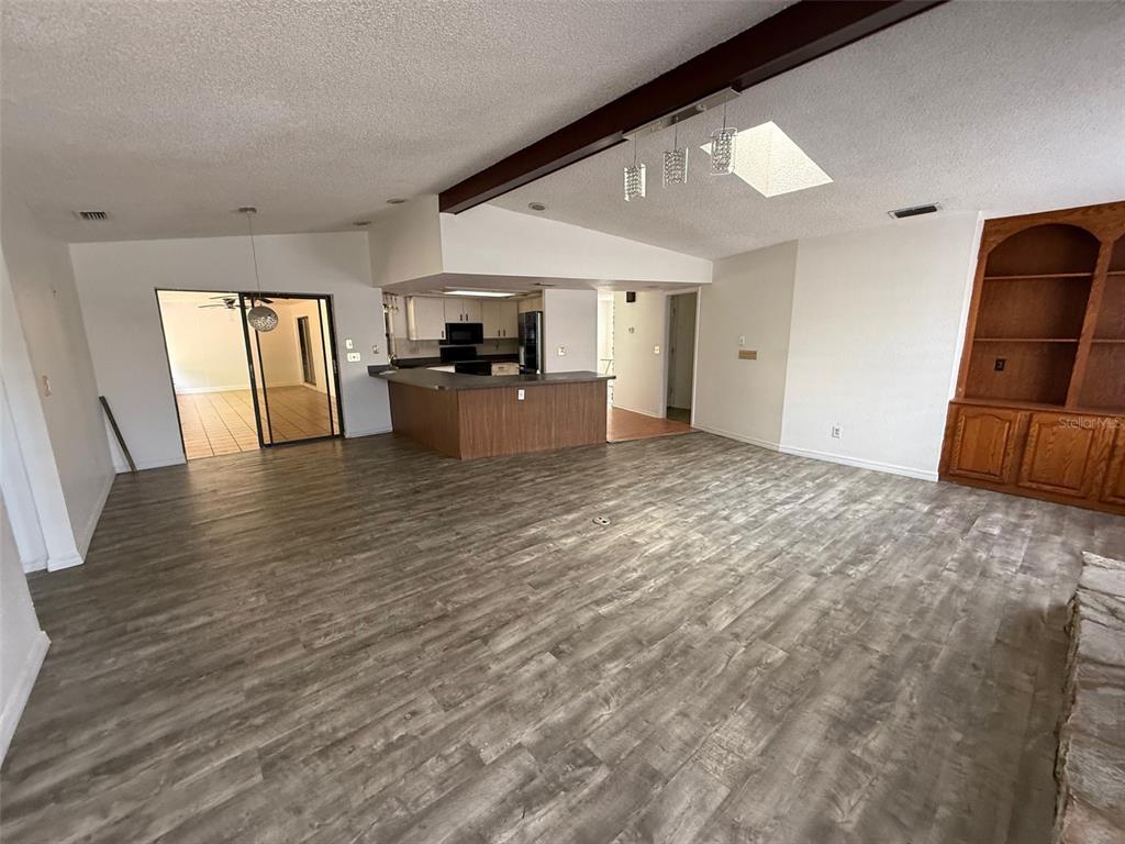 A spacious living area features wood-look flooring, a kitchen peninsula, and built-in wooden shelving — 5312 SUWANNEE ROAD, WEEKI WACHEE, FL