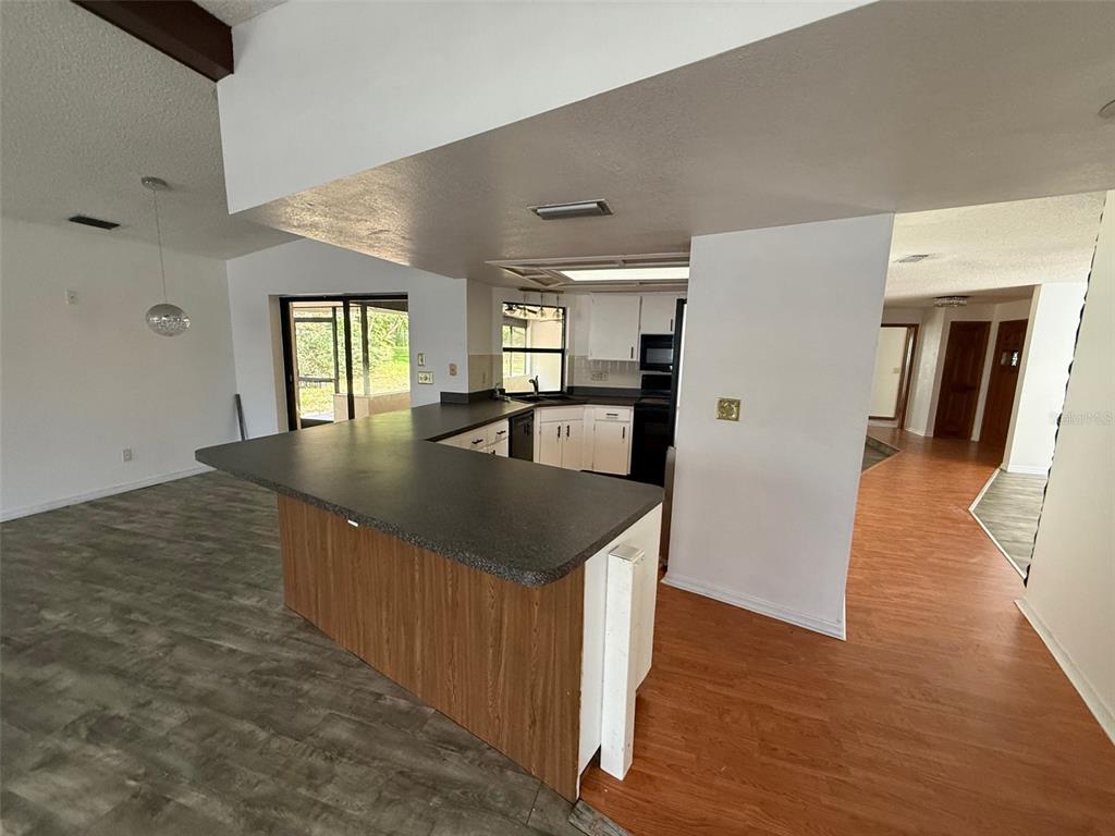 A kitchen with a dark countertop peninsula overlooks a living area with wood-look flooring — 5312 SUWANNEE ROAD, WEEKI WACHEE, FL