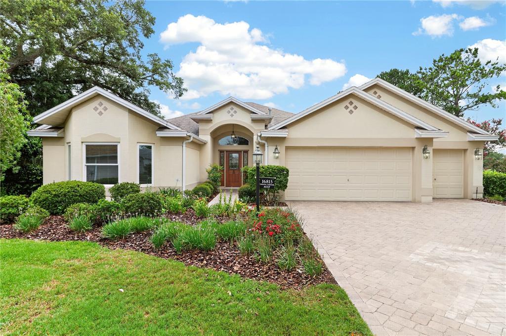 A single-story suburban house with a beige stucco exterior, a three-car garage, and landscaping — 16815 SE 85TH BELKNAP AVENUE, THE VILLAGES, FL