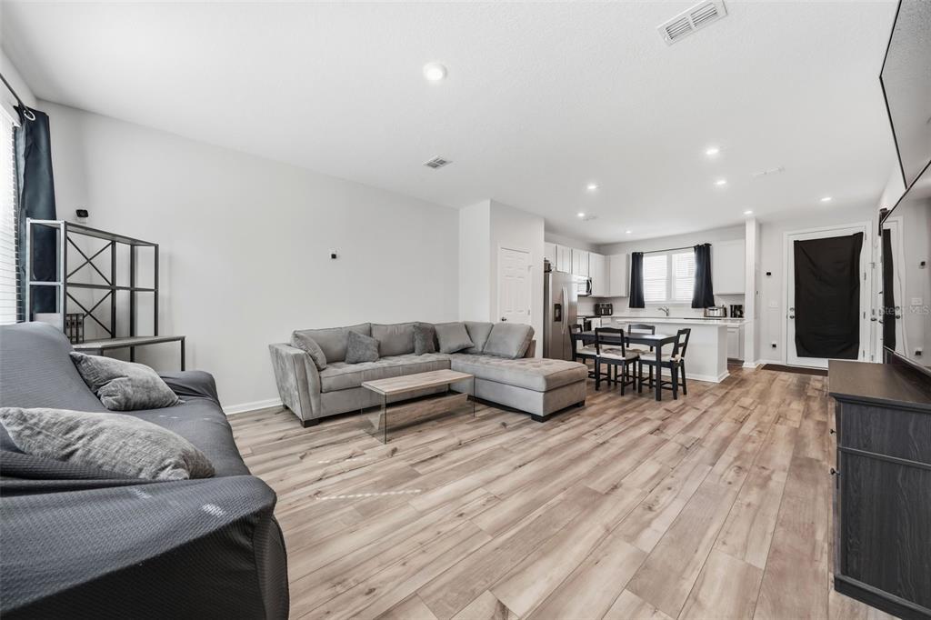 An open-concept living room and kitchen featuring light wood-look flooring and gray sectional sofas — 46 AXEL FALL DRIVE, ST JOHNS, FL