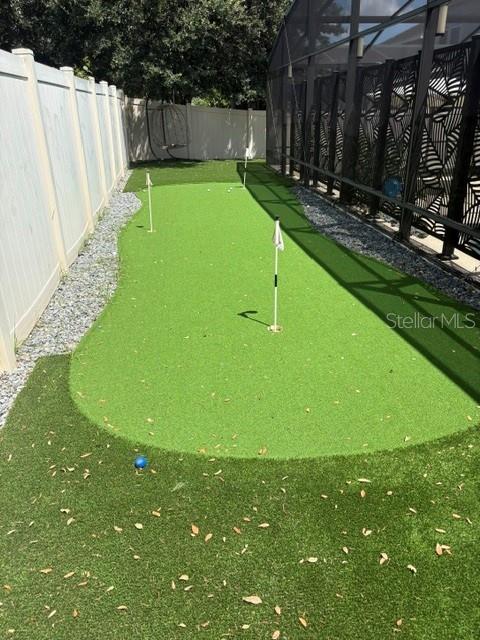 A backyard putting green with two flagsticks sits between a white fence and a pool enclosure — 14776 MAGNOLIA RIDGE LOOP, WINTER GARDEN, FL