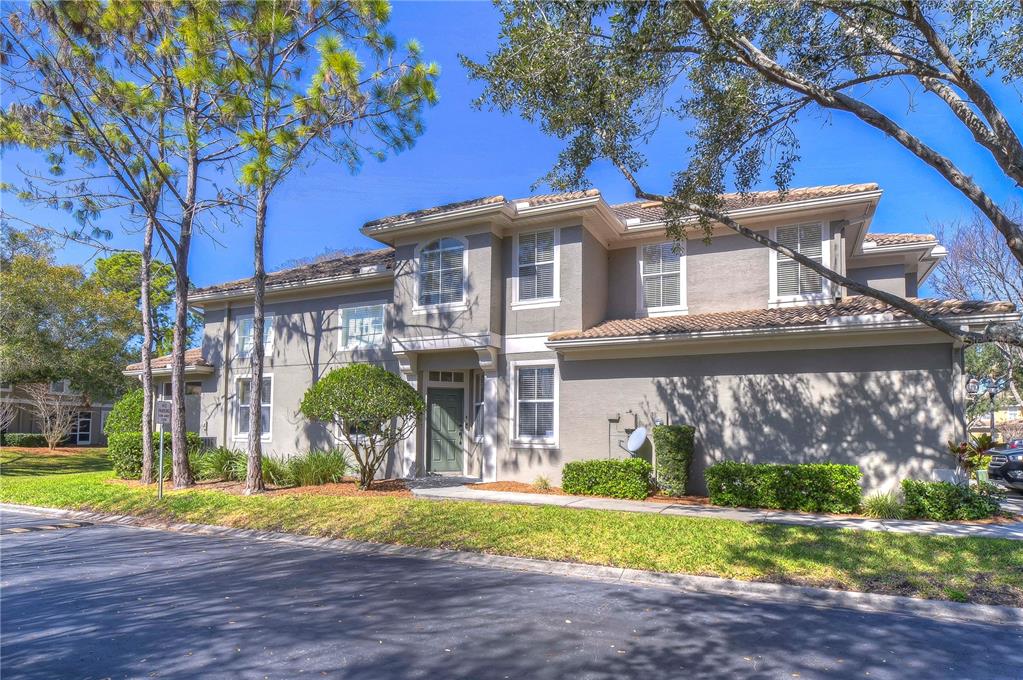 A two-story gray stucco townhouse with a tile roof and a green front door — 3292 COVERED BRIDGE DRIVE E, DUNEDIN, FL