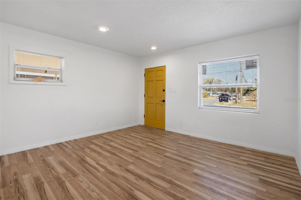 An empty room features white walls, light wood-look flooring, a yellow door, and two windows — 6146 DAHLIA DRIVE, ORLANDO, FL