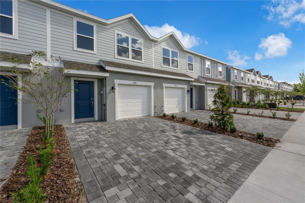 A row of gray townhouses features blue front doors, white garage doors, and paver driveways — 3040 JESSAMINE DRIVE, TAVARES, FL