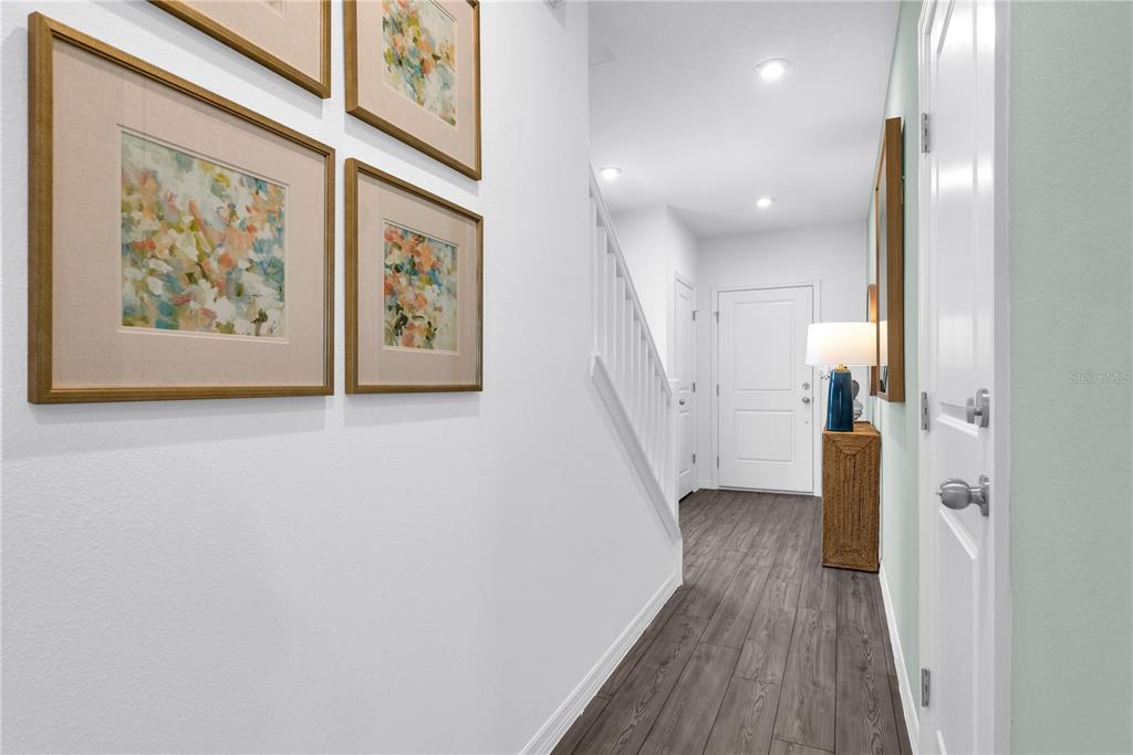 A hallway with wood-look flooring, white walls, a staircase, and framed artwork on the left — 3040 JESSAMINE DRIVE, TAVARES, FL