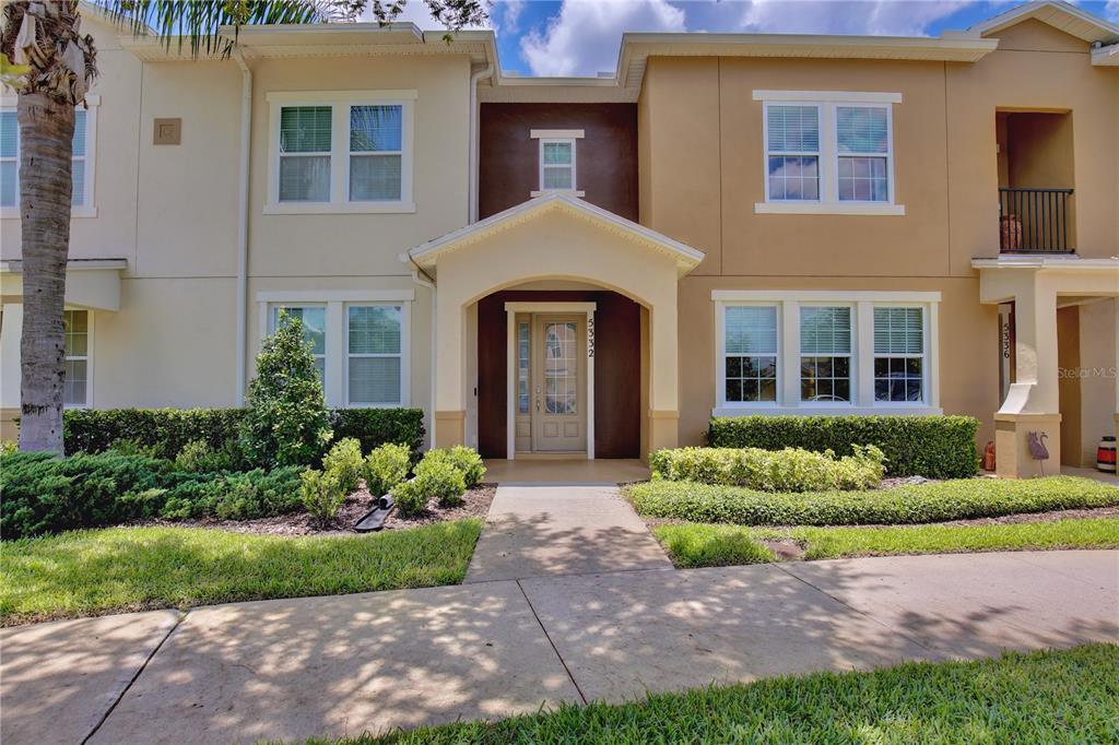 A two-story townhouse exterior with a tan facade, a covered entryway, and landscaped front yard — 5332 FACTORS WALK DRIVE, SANFORD, FL