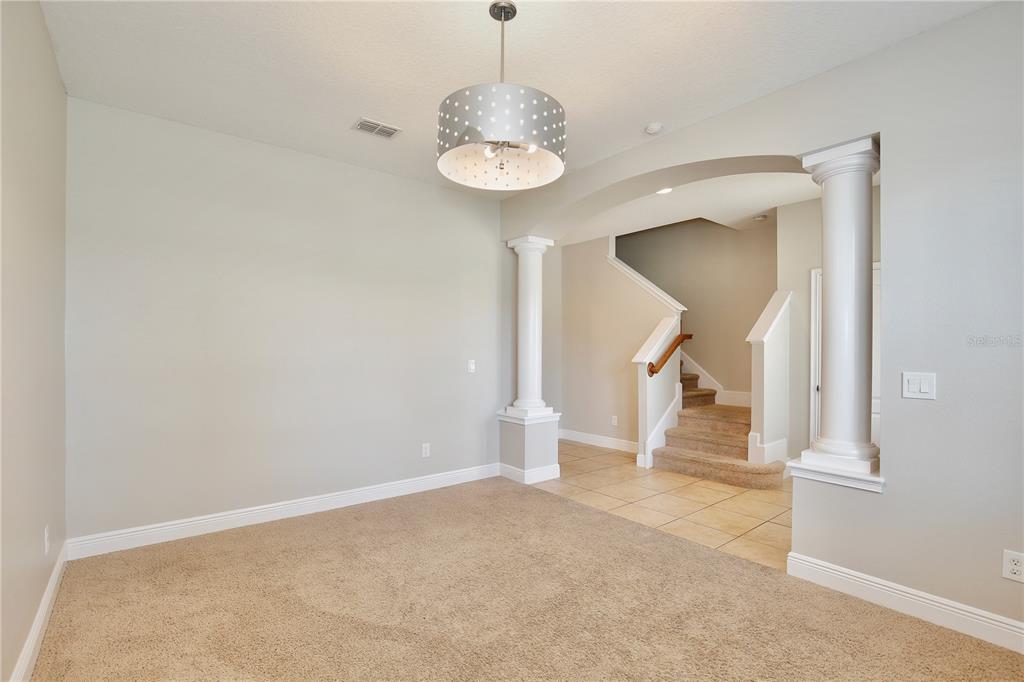 A carpeted dining room features a drum pendant light, white columns, and an adjacent staircase — 5332 FACTORS WALK DRIVE, SANFORD, FL