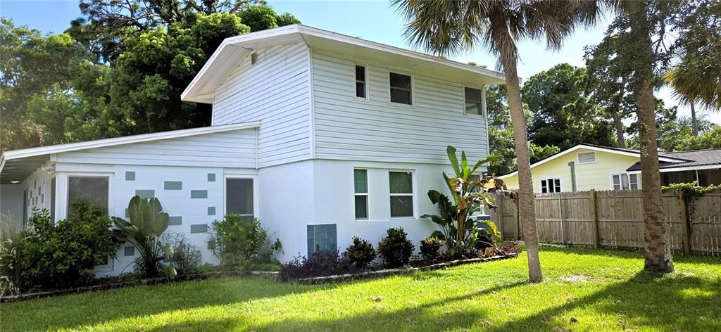 A two-story white house with horizontal siding and a flat-roofed extension sits on a lawn — 415 VENETIAN DRIVE, CLEARWATER, FL