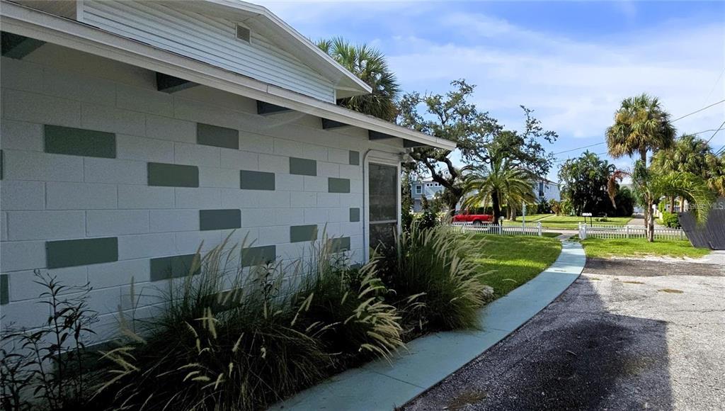 A side view of a white concrete block house with decorative green rectangles and landscaping — 415 VENETIAN DRIVE, CLEARWATER, FL
