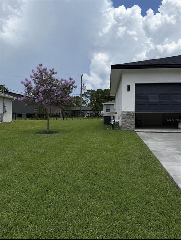A side view of a house with a garage, a lawn, and a flowering tree — 1681 WELLAND STREET SE, PALM BAY, FL