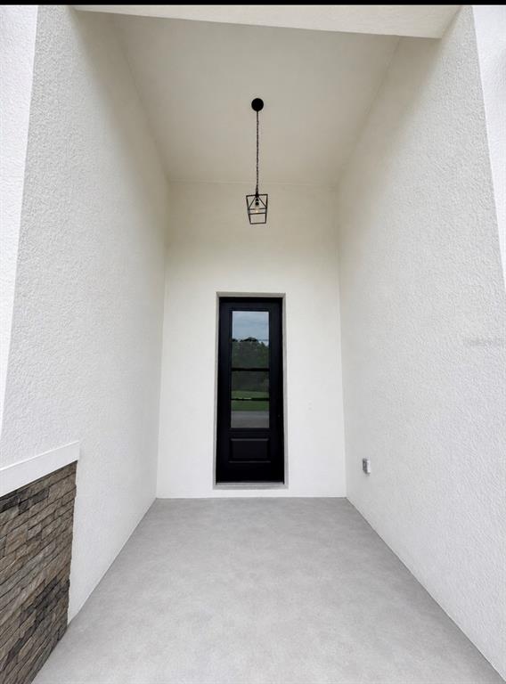 A covered entryway features white stucco walls, a gray concrete floor, and a black door — 1681 WELLAND STREET SE, PALM BAY, FL