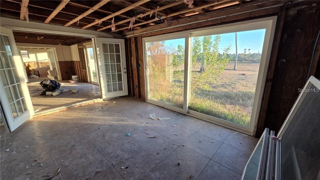 An unfinished room features exposed ceiling joists, tiled flooring, and large sliding glass doors — 4020 HEADSAIL DRIVE, NEW PORT RICHEY, FL