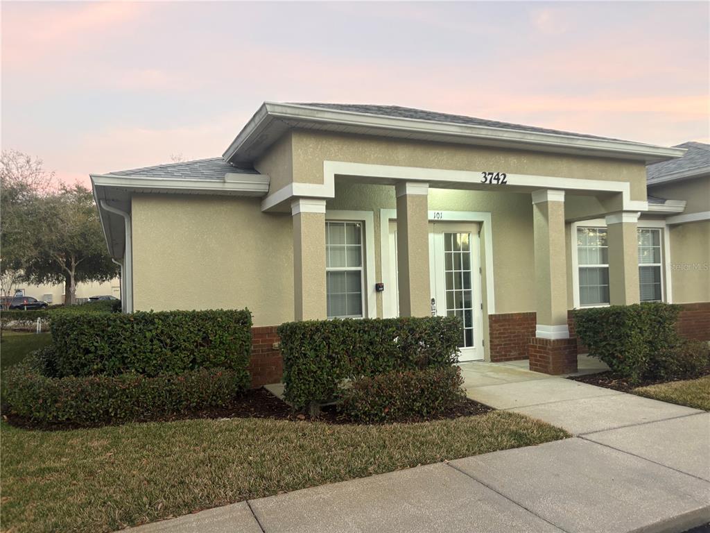 A single-story commercial building with a tan stucco exterior, brick accents, and a covered entrance — 3742 TURMAN LOOP UNIT 101, WESLEY CHAPEL, FL