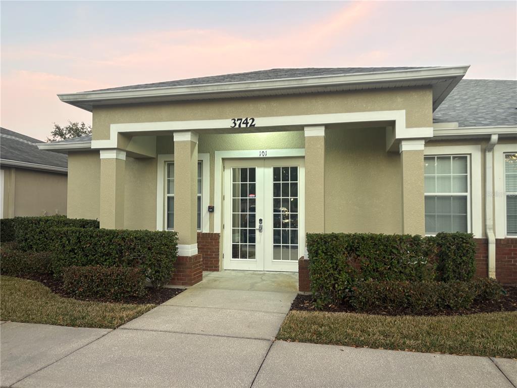 The exterior of a tan building features a covered entrance with double glass doors — 3742 TURMAN LOOP UNIT 101, WESLEY CHAPEL, FL