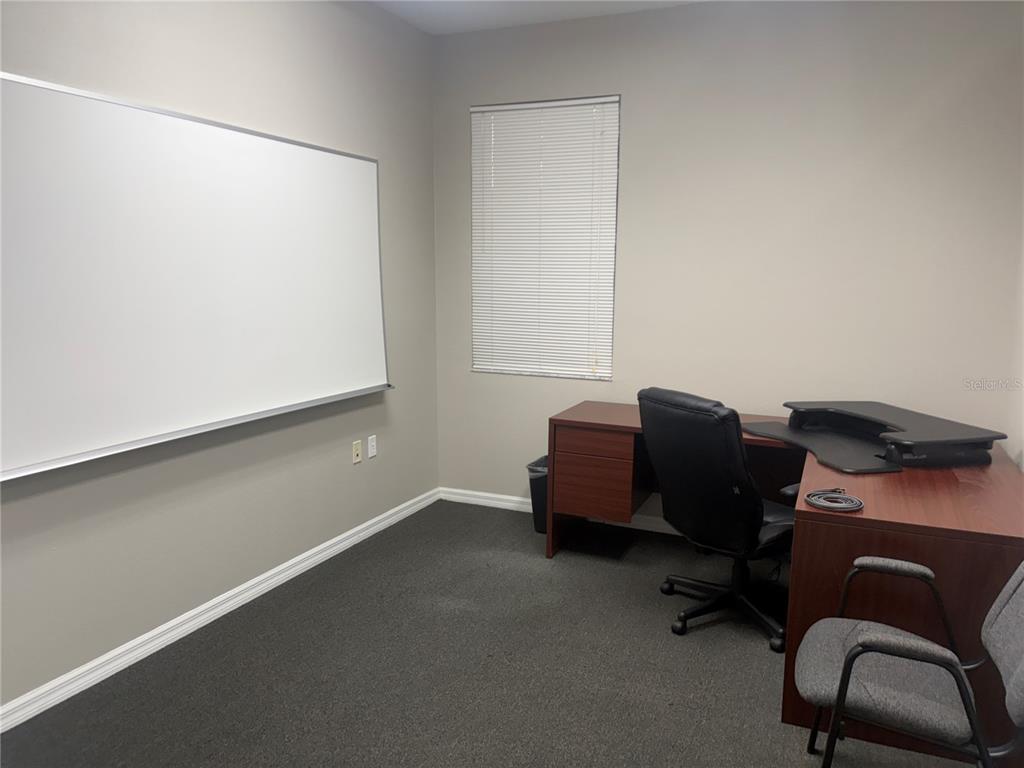 An office room features a large whiteboard, a desk with a chair, and carpeted flooring — 3742 TURMAN LOOP UNIT 101, WESLEY CHAPEL, FL