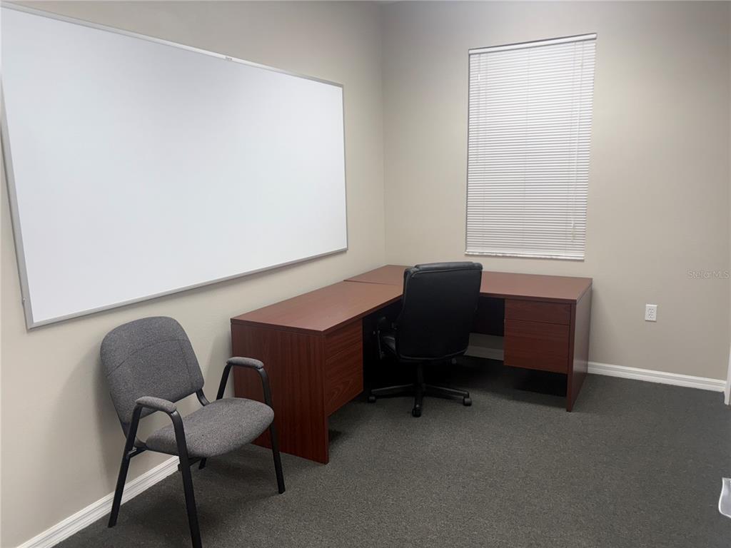 An office features a wooden L-shaped desk, a black chair, a guest chair, and whiteboard — 3742 TURMAN LOOP UNIT 101, WESLEY CHAPEL, FL