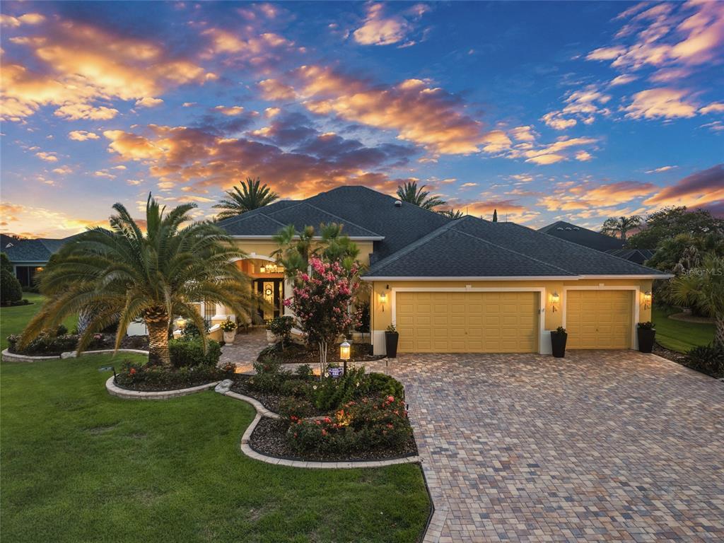 An exterior view of a single-story house with a paved driveway and a sunset sky — 622 LAUREL RUN, THE VILLAGES, FL