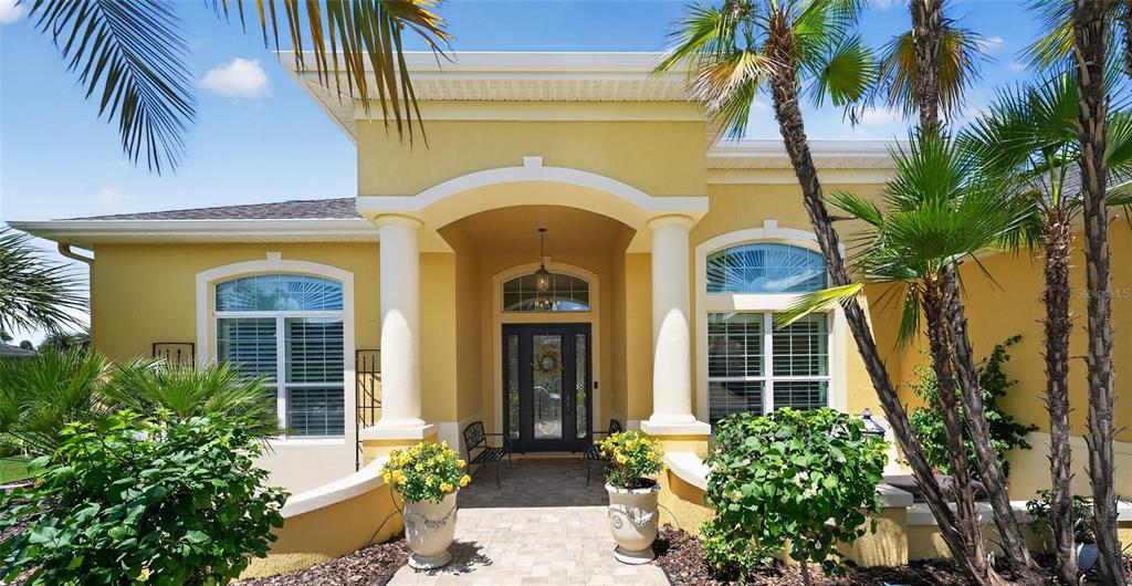 The exterior of a yellow house features a covered entryway with columns and palm trees — 622 LAUREL RUN, THE VILLAGES, FL