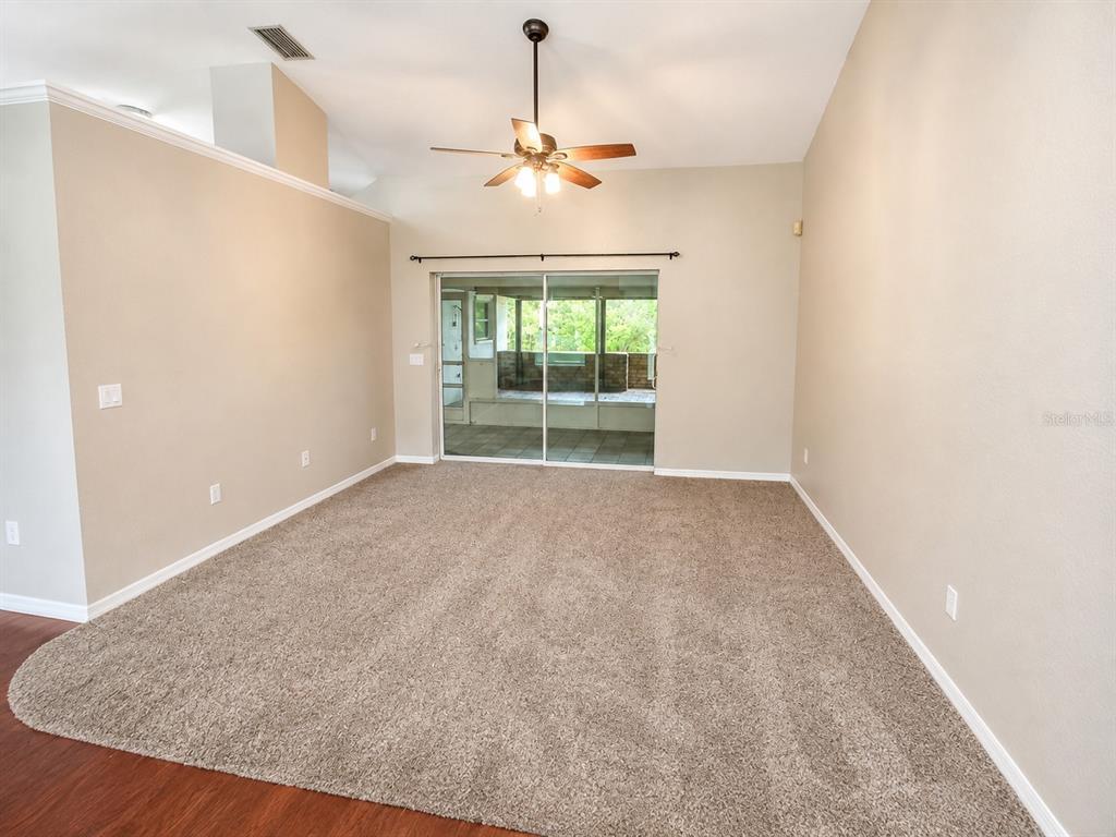 An empty living room features beige walls, brown carpeting, a ceiling fan, and sliding glass doors — 3095 SCHOMER STREET, NORTH PORT, FL