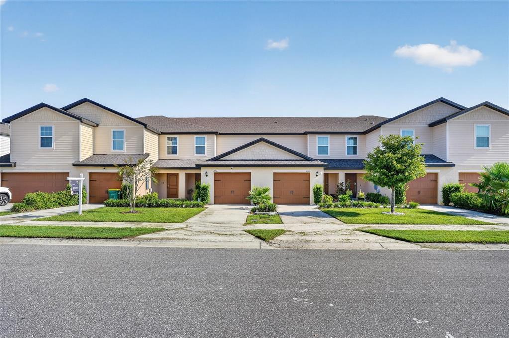 A row of attached townhouses with tan siding, brown garage doors, and green front lawns — 1556 WYNFORD CIRCLE, TAVARES, FL