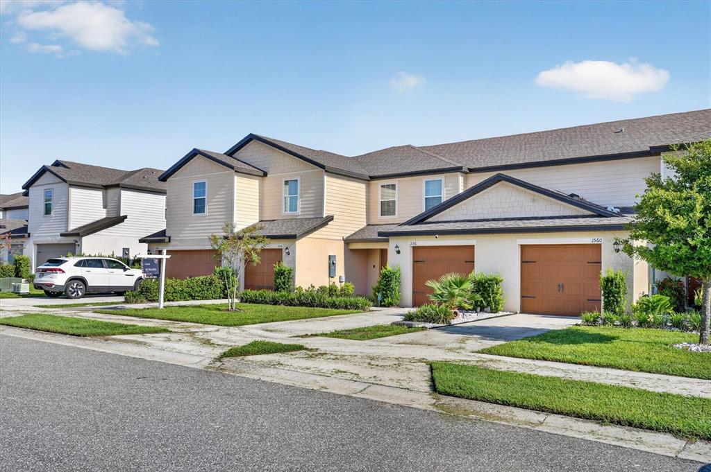 A row of two-story townhomes with tan siding, brown garage doors, and a paved driveway — 1556 WYNFORD CIRCLE, TAVARES, FL