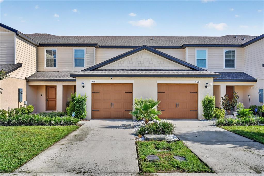 The exterior view shows two attached townhomes with tan siding, brown garage doors, and driveways — 1556 WYNFORD CIRCLE, TAVARES, FL