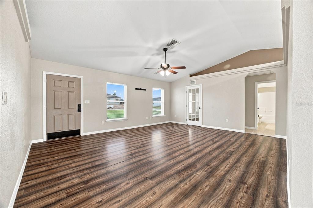 An empty living room features wood-look flooring, a vaulted ceiling with a fan, and beige walls — 10143 SE 122ND LANE, BELLEVIEW, FL