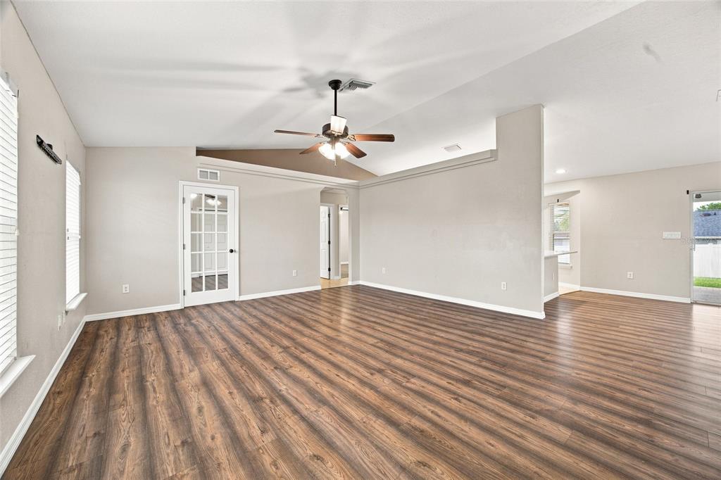 A spacious living room features wood-look flooring, a vaulted ceiling with a fan, and French doors — 10143 SE 122ND LANE, BELLEVIEW, FL