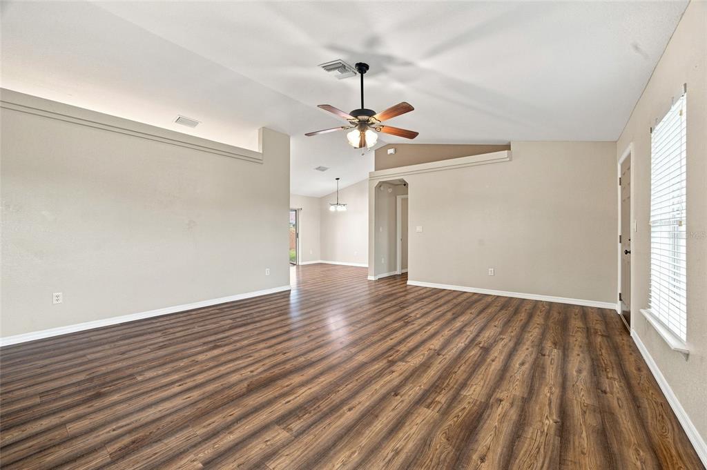 An empty living room features wood-look laminate flooring, a ceiling fan, and beige walls — 10143 SE 122ND LANE, BELLEVIEW, FL