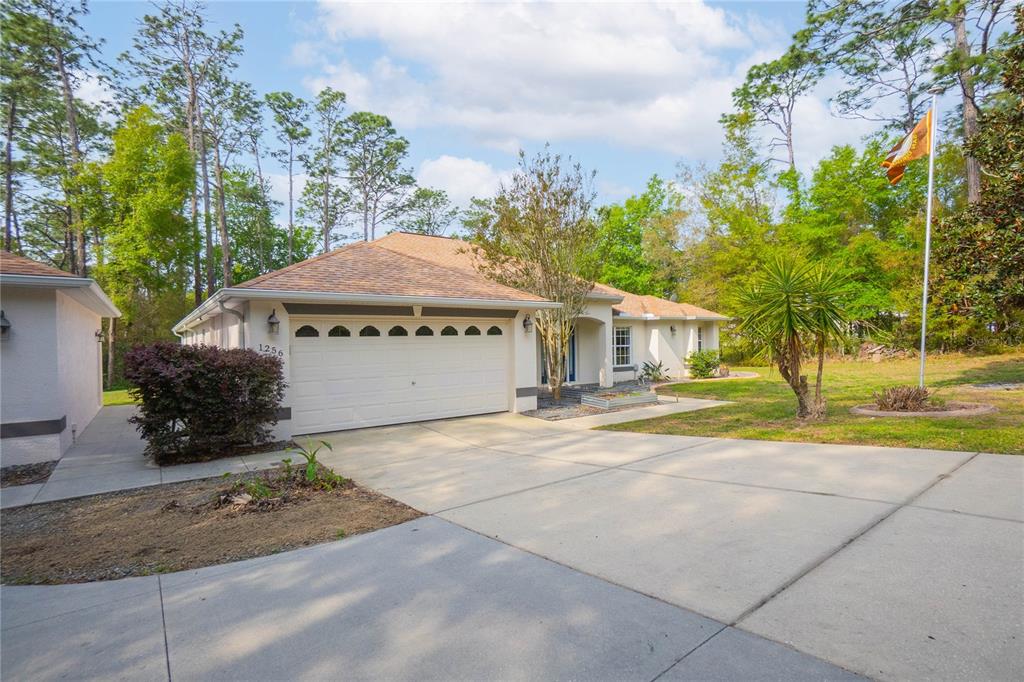 A single-story house with a white garage, a concrete driveway, and surrounding trees — 1256 W SPHERE PLACE, BEVERLY HILLS, FL
