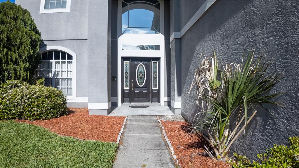 A concrete walkway leads to the dark front door of a gray stucco house — 2890 CULLENS COURT, OCOEE, FL