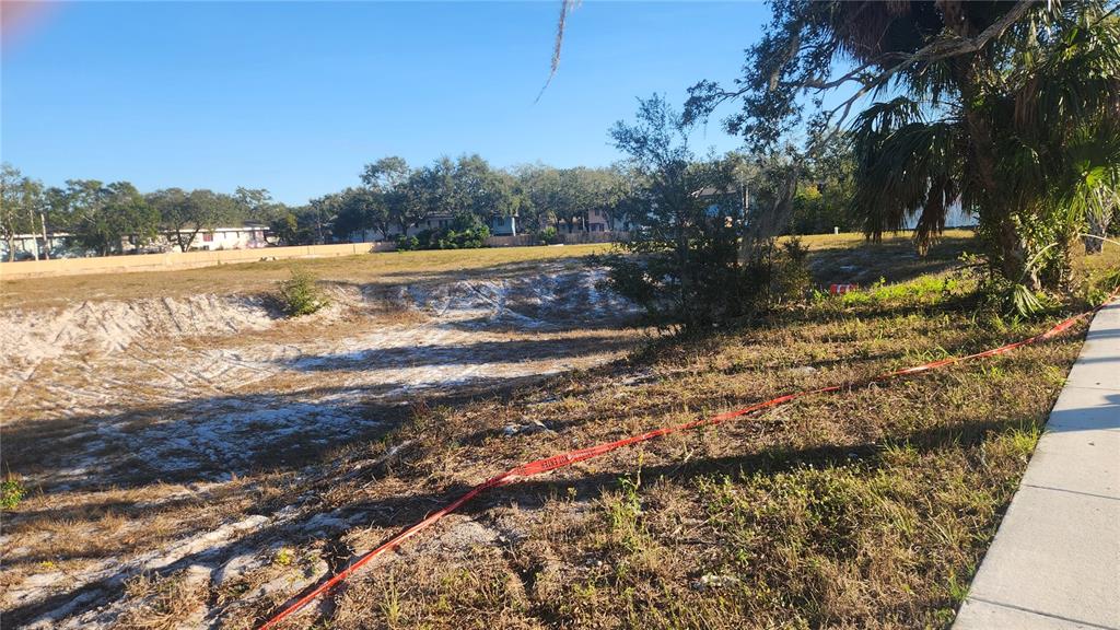A vacant, sandy lot with a depression is bordered by a sidewalk and trees — DRUID ROAD E, CLEARWATER, FL