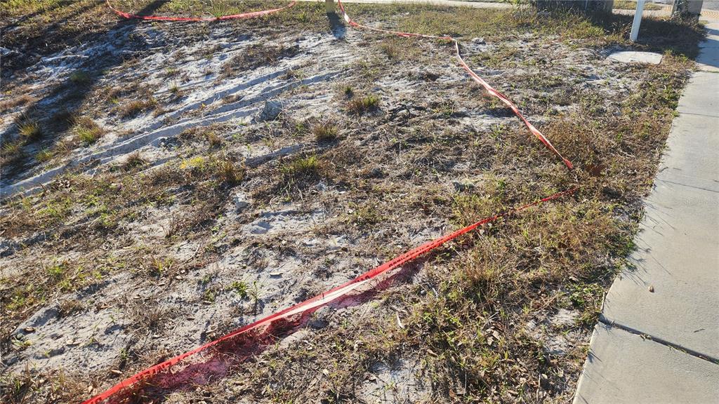 A vacant, sandy residential lot is marked off with red caution tape near a sidewalk — DRUID ROAD E, CLEARWATER, FL
