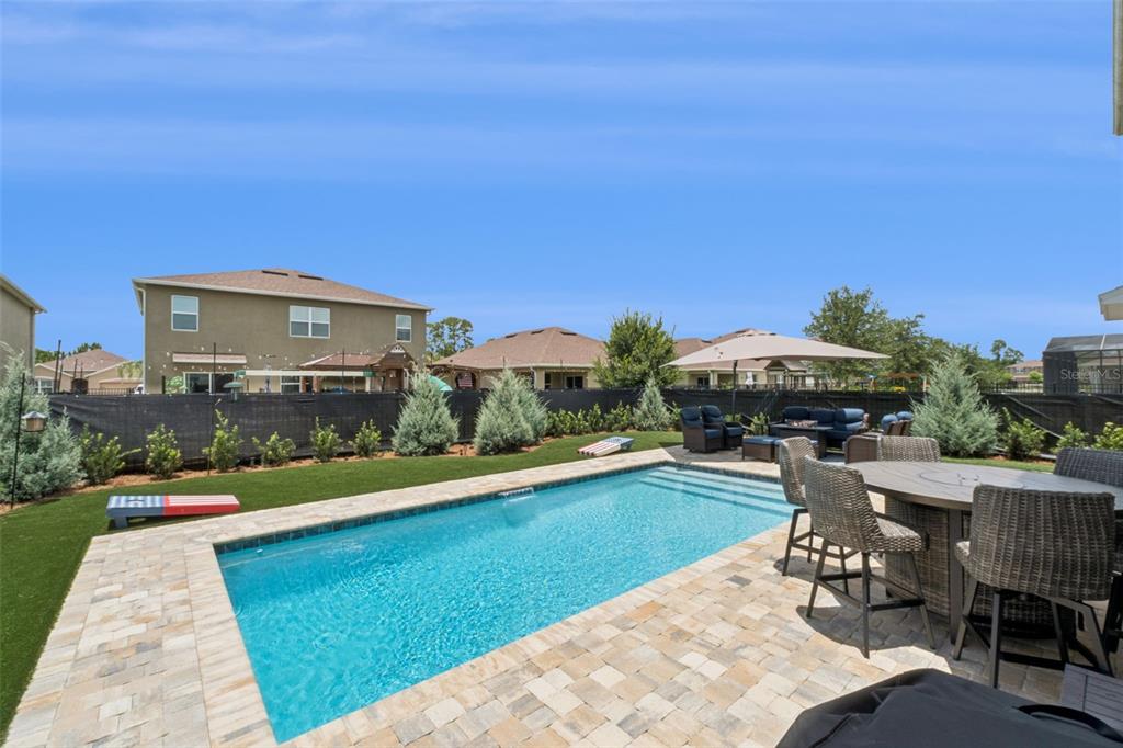 A backyard features a rectangular swimming pool, a patio with dining furniture, and artificial turf — 358 LAZIO CIRCLE, DEBARY, FL